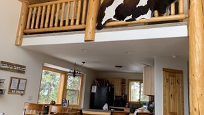 Un vaste espace de vie aménagé dans un style loft, avec un haut plafond doté d’un ventilateur, un escalier en bois et un coin repas équipé de tabourets de bar.