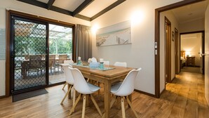 A dining area with a wooden table and white chairs, a sliding glass door leading to an outdoor patio, and a painting on the wall. - Inlet Dreaming - Inlet Side Inverloch (INVERLOCH)