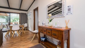 A dining area with a wooden table and chairs, a wooden cabinet with drawers, a mirror, and a vase with flowers. - Inlet Dreaming - Inlet Side Inverloch (INVERLOCH)