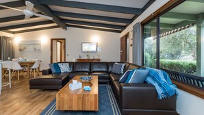 A modern living room with a sectional sofa, a wooden coffee table, and a dining area with a table and chairs. - Inlet Dreaming - Inlet Side Inverloch (INVERLOCH)