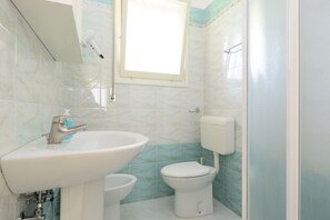 A bathroom with a sink, toilet, and a window.