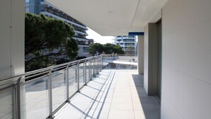 A modern building with a glass balcony, white tiled floors, and a view of other buildings and trees. - Appartamenti Nashira (Lignano Sabbiadoro)