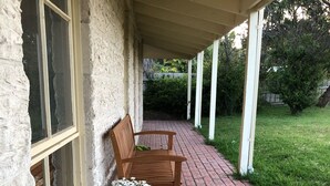 Une véranda couverte avec un chemin en briques, un banc en bois et deux plantes en pot ornées de fleurs.