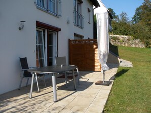 A patio with a table and chairs, a wooden fence, and a white umbrella.