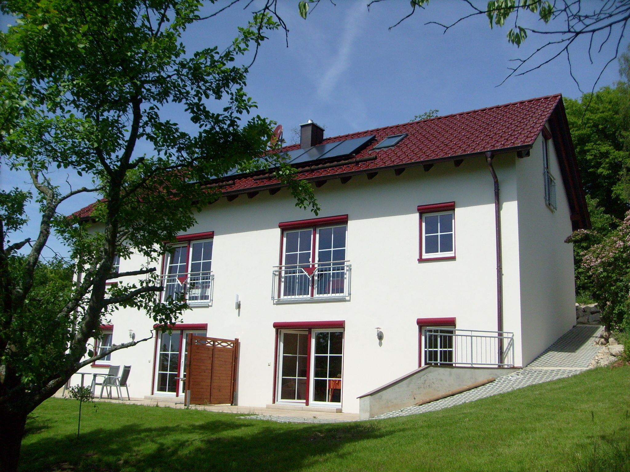 A two-story house with a red-tiled roof, white walls, and multiple windows with red trim.