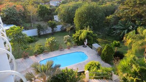 A residential area with a swimming pool surrounded by lush greenery and a view of distant hills. - Casa Anonna - Stunning oceans views and pool! (Vieques)