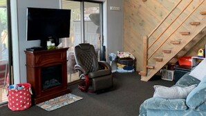 A living room with a fireplace, a television, a large window, and a wooden staircase. - Chautauqua lakefront cottage🐠GREAT LOCATION 🐠Pet friendly (Jamestown)