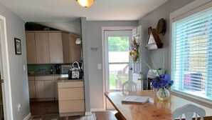A kitchen with wooden flooring, a wooden bench, and a white chair. There is a window with blinds and a door leading outside. - Chautauqua lakefront cottage🐠GREAT LOCATION 🐠Pet friendly (Jamestown)