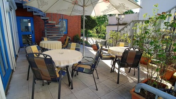 Un patio al aire libre con mesas y sillas redondas, una escalera y plantas en macetas.