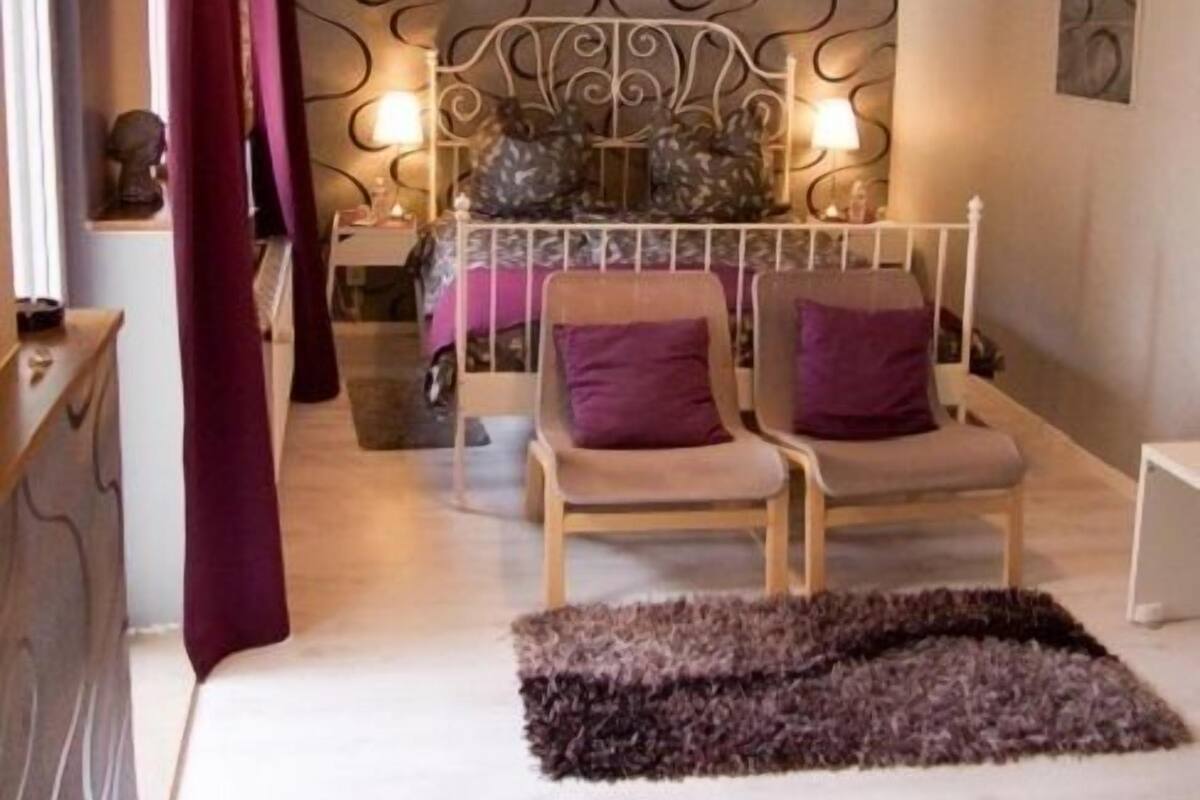 A bedroom with a bed, two chairs, a nightstand, and a decorative wall.