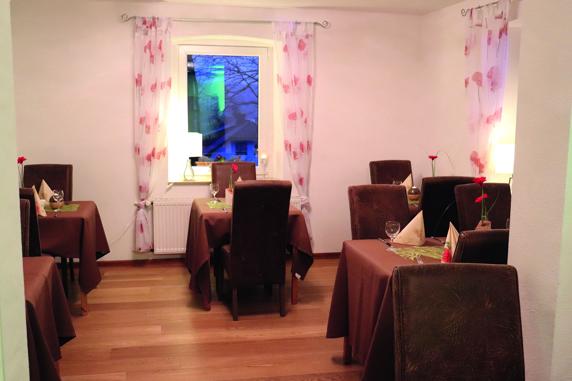 A dining area with multiple tables and chairs, a window with curtains, and a radiator.