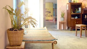 Una habitación con un banco de madera, una mesita, una planta en maceta y un mueble con objetos decorativos.