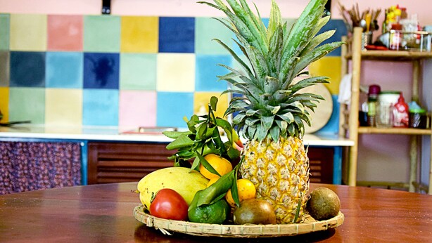 Una cesta de fruta sobre una mesa, con un colorido revestimiento de azulejos al fondo.