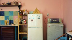 Una cocina con refrigerador, microondas y pileta. Hay repisas con frascos y un mueble de madera.