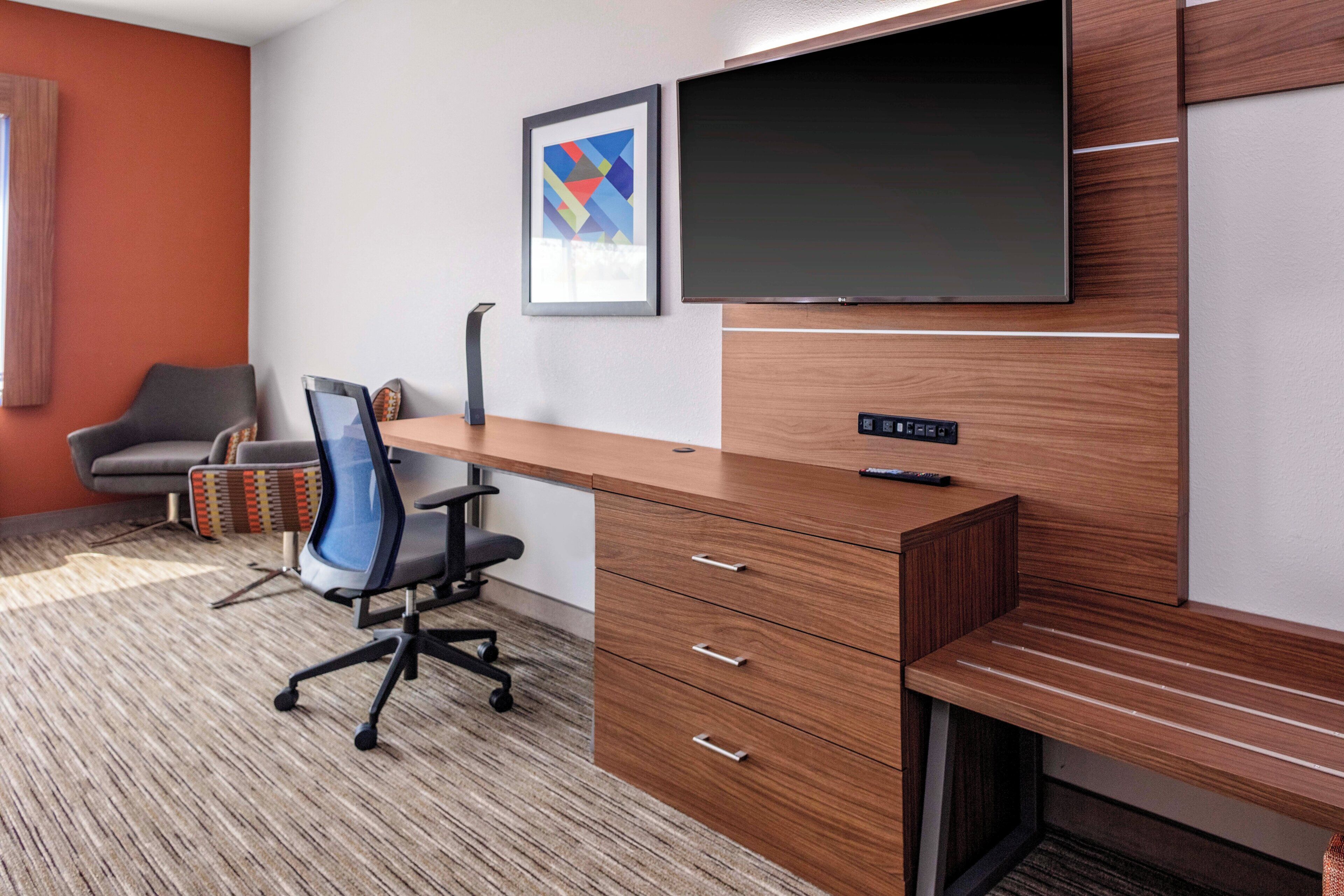 A modern office space with a wooden desk, a chair, a television, and a framed picture on the wall.