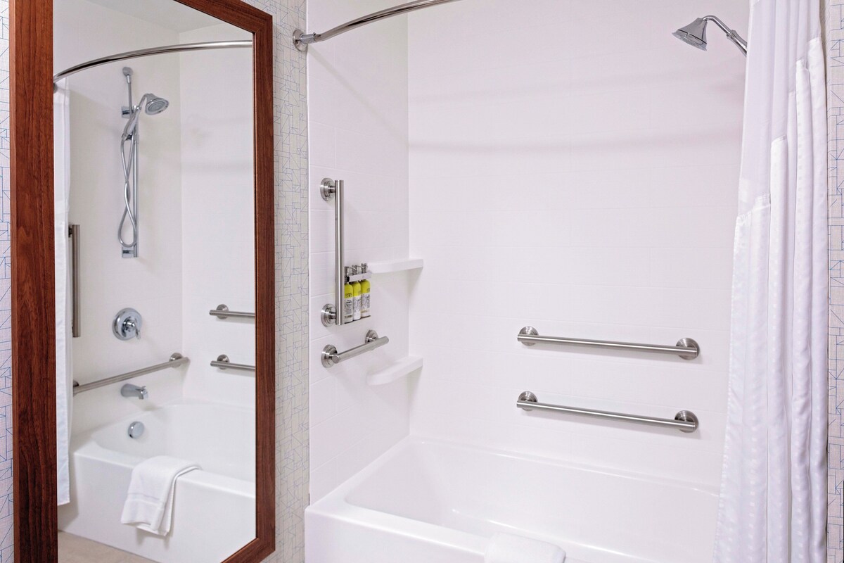 A bathroom with a bathtub, a shower, and a toilet. There are grab bars installed for safety.