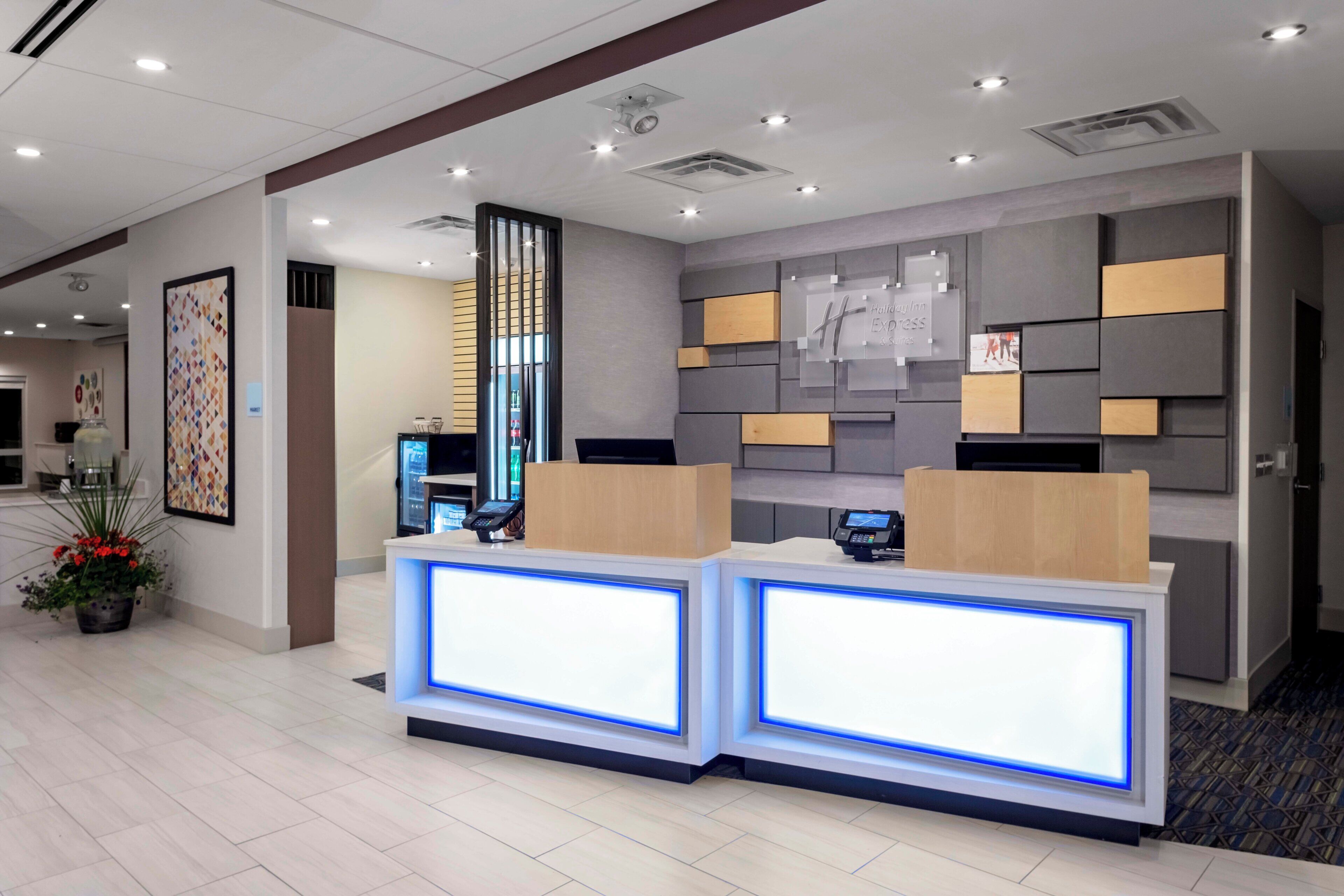 A hotel reception area with a modern design, featuring a reception desk, a digital display, and a wall-mounted information board.