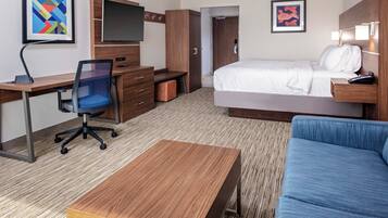 A hotel room with a bed, a desk with a chair, a TV, and artwork on the walls.
