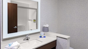 Un bany amb un mirall gran, un lavabo blanc, un armari de fusta i un escurapulides.