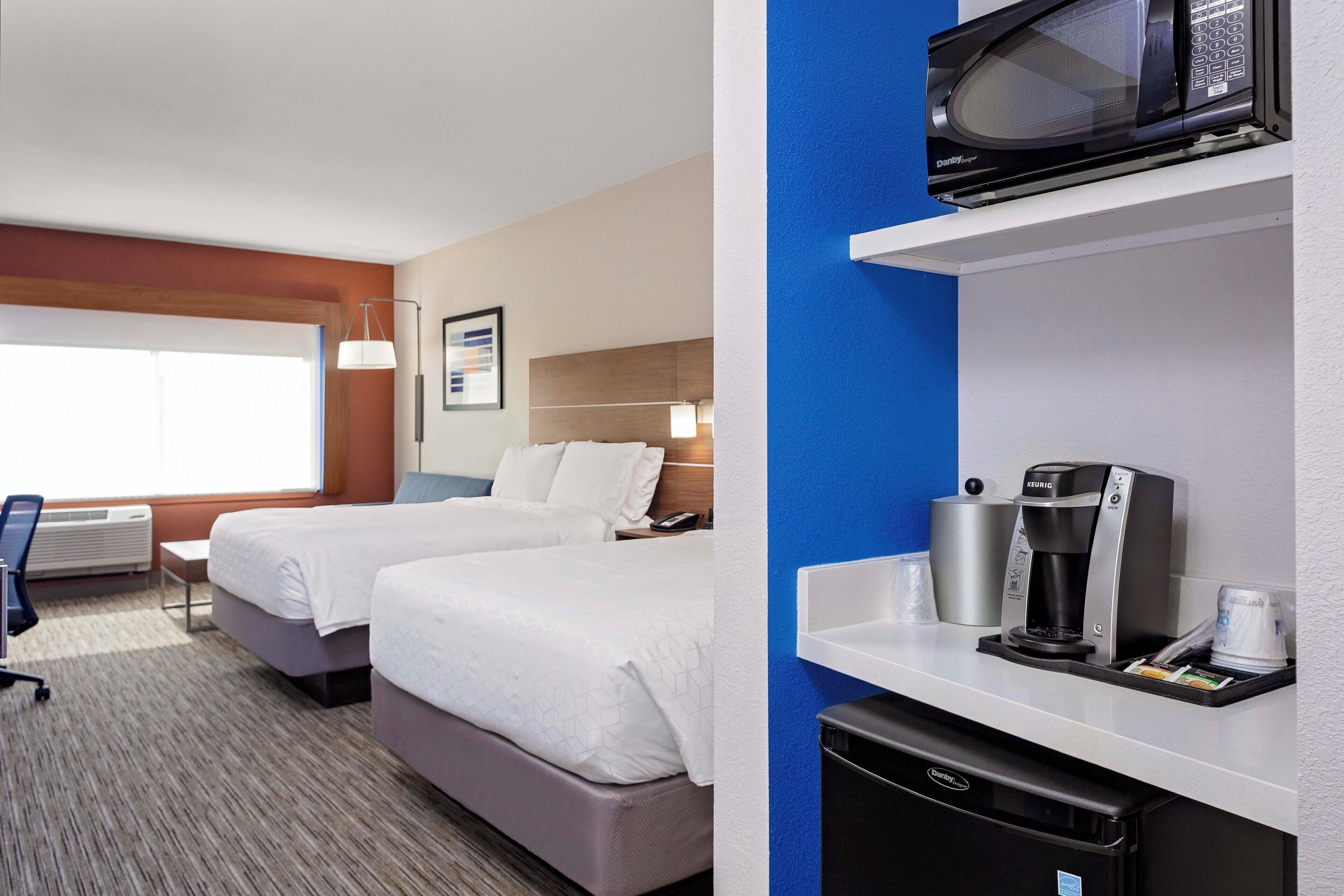 A hotel room with two beds, a microwave, a coffee maker, and a small refrigerator.
