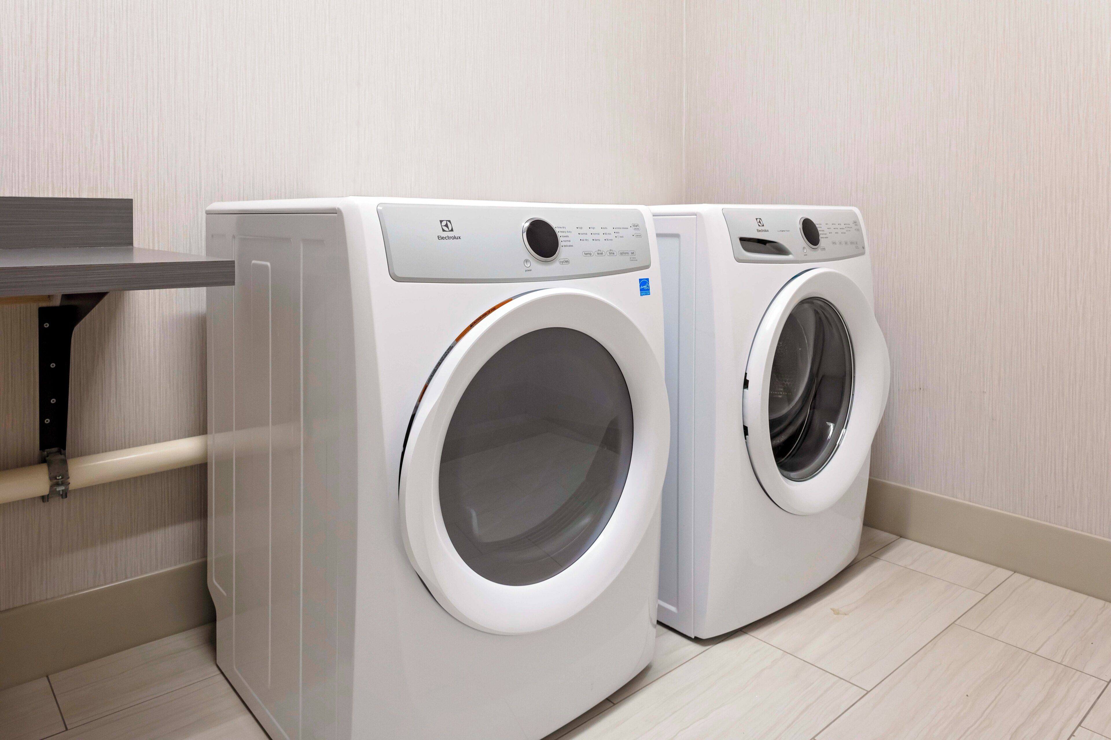 Two front-loading washing machines in a laundry room with a wooden floor and a metal shelf.