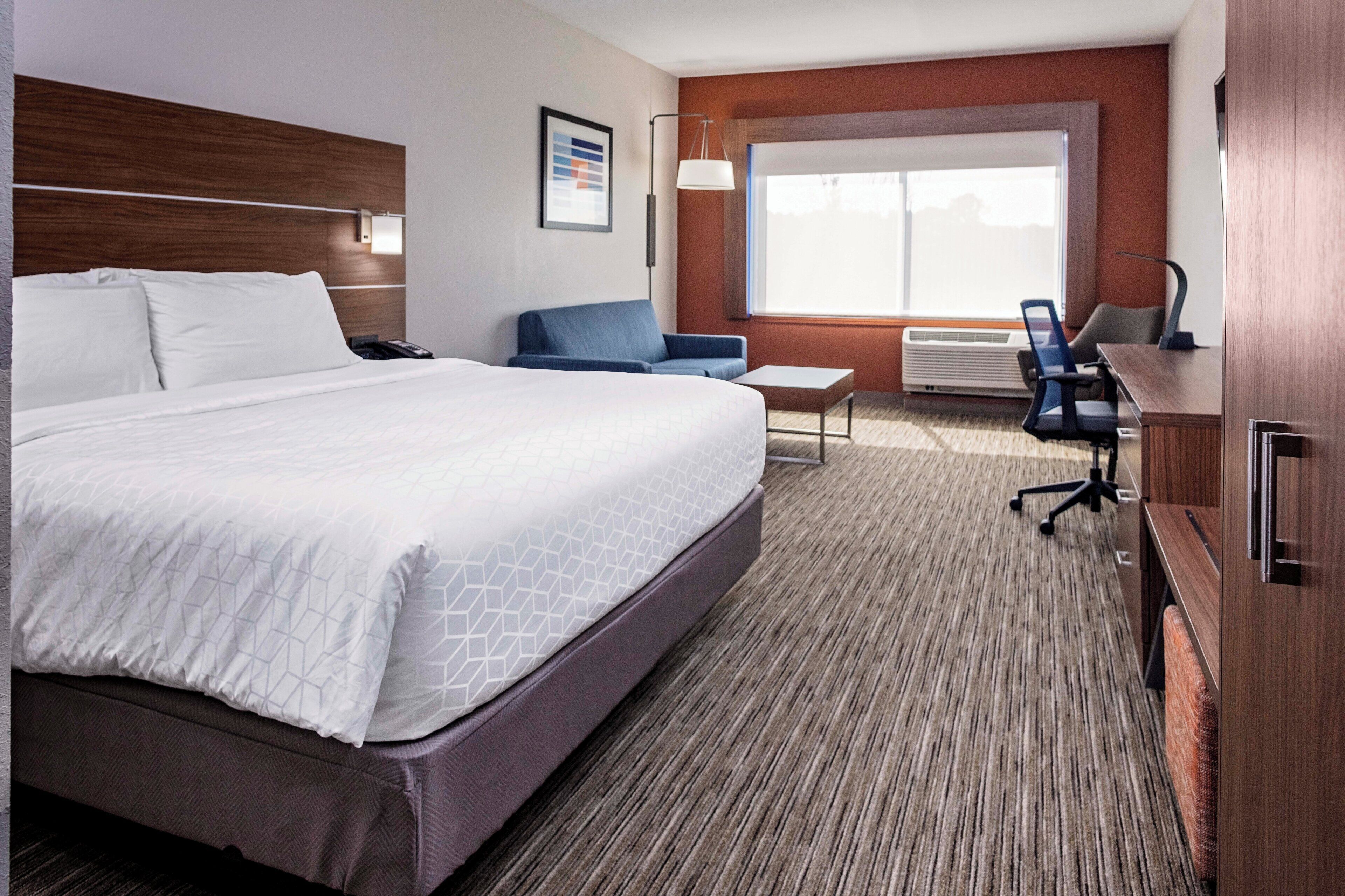 A hotel room with a large bed, a desk, a chair, and a window.