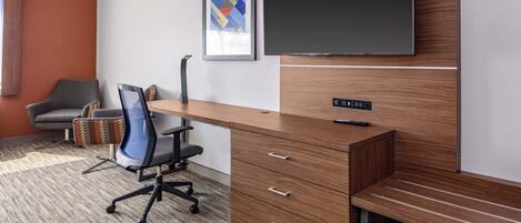 A modern office space with a wooden desk, a chair, a framed picture, and a flat-screen TV mounted on the wall.