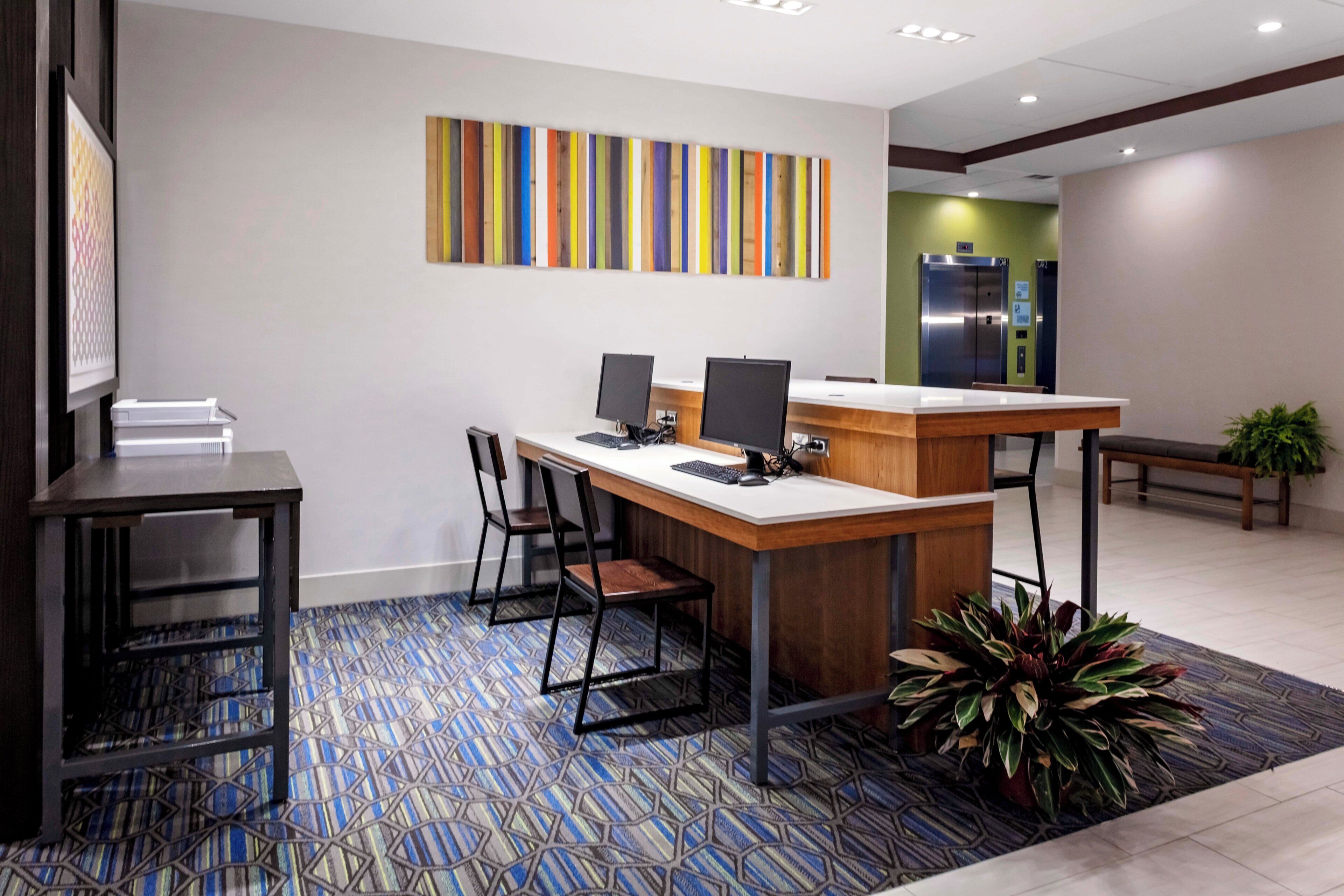 A reception desk with two computer monitors, a printer, and a seating area with chairs.