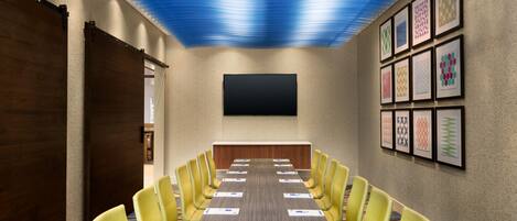 A conference room with a long table, yellow chairs, a flat-screen TV, and framed artwork on the walls.
