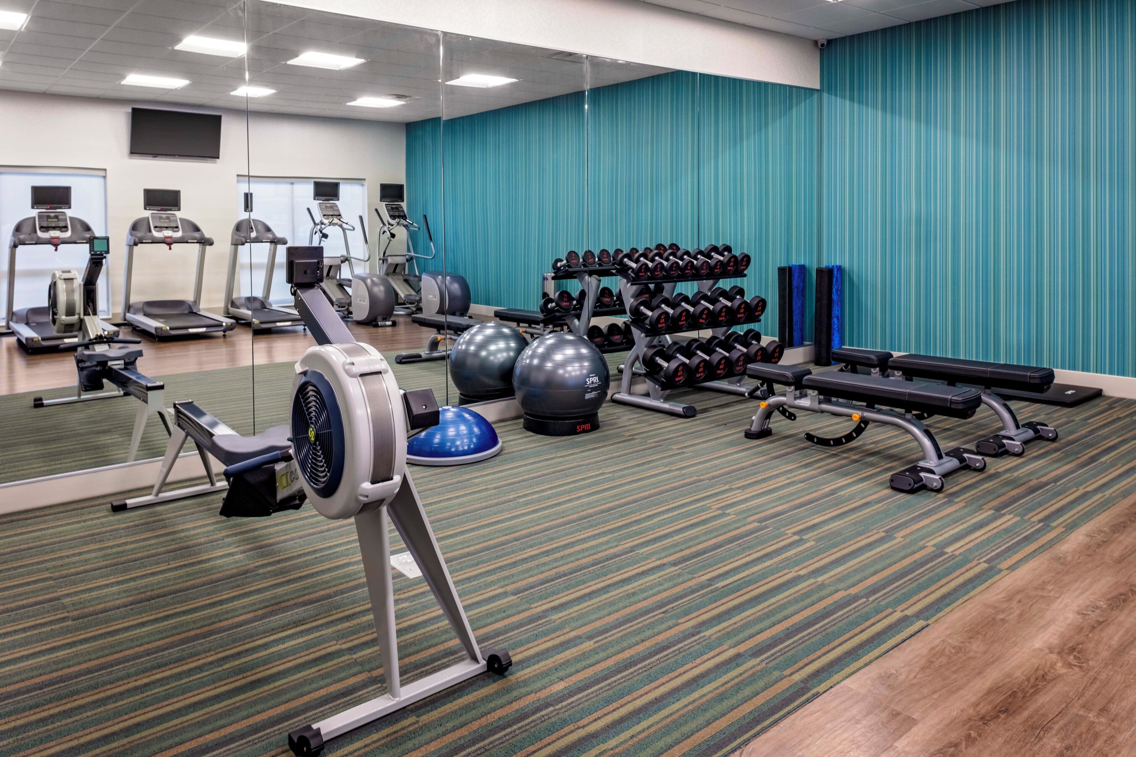 A gym with treadmills, elliptical machines, weight benches, and free weights.