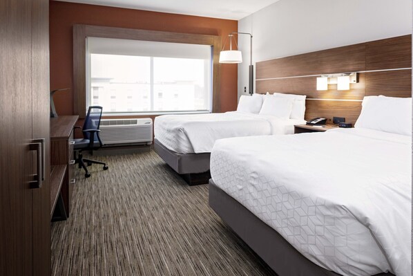 A hotel room with two beds, a desk, a chair, a lamp, and a large window.