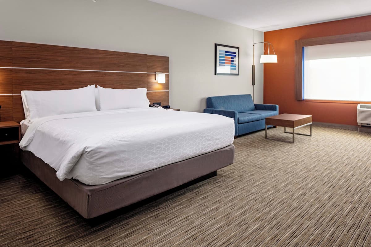 Moderni hotellihuone, jossa on suuri sänky, sininen nojatuoli, pieni pöytä ja suuri ikkuna.