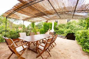 An outdoor patio with a wooden table and chairs, a thatched roof, and surrounding greenery. - Casa Rosa (Assisi)