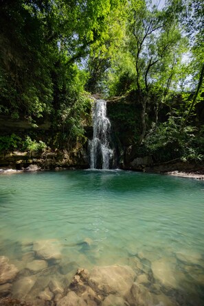 A waterfall cascading into a clear pool surrounded by lush greenery. - Casa Rosa (Assisi)