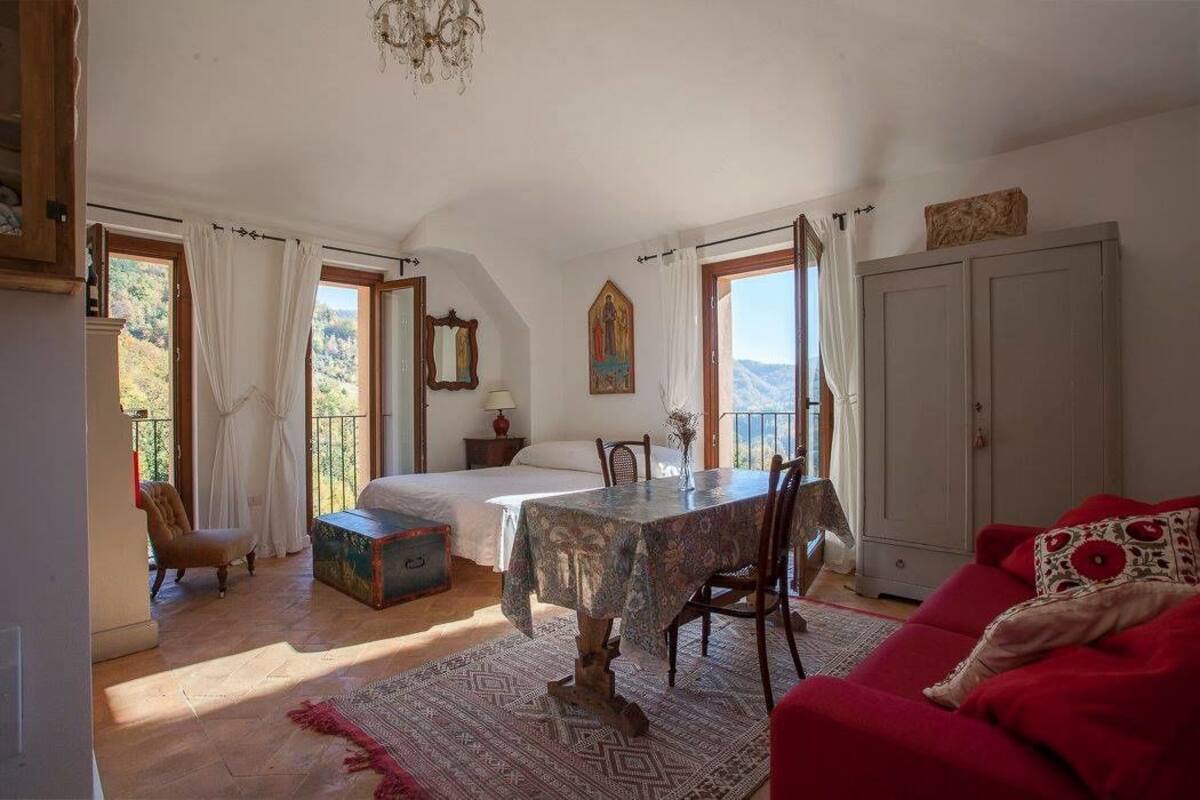 A bedroom with a bed, a table, a red sofa, and a view of the outdoors.