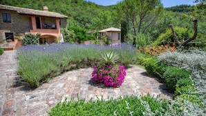 A stone house with a garden featuring lavender and pink flowers, surrounded by greenery and trees. - Casa Rosa (Assisi)