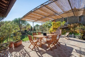 An outdoor patio with a table and chairs, surrounded by potted plants and a stone building. - Casa Rosa (Assisi)