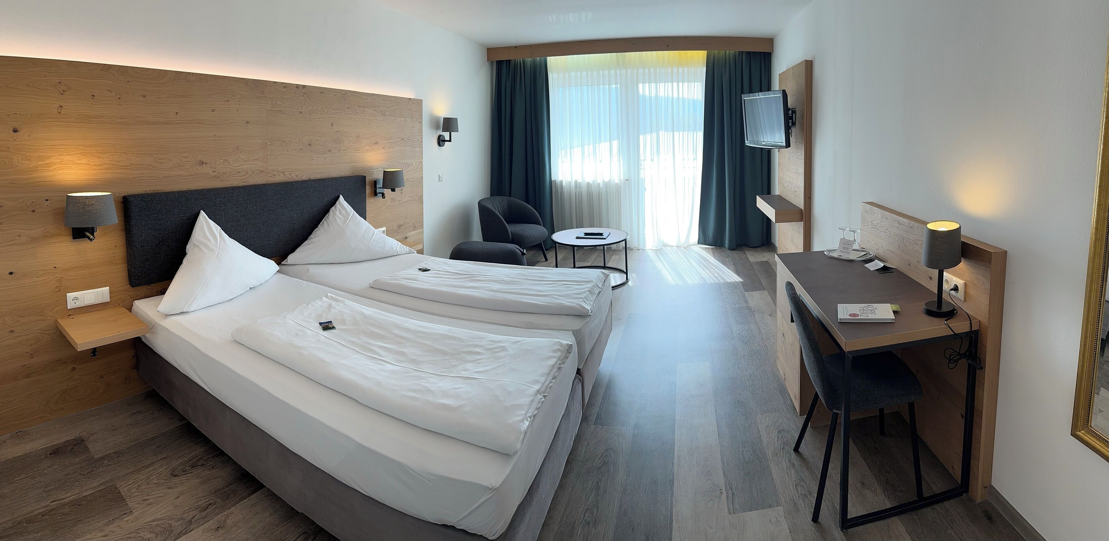 Habitación de hotel con una cama grande, un escritorio, una silla, un televisor y una ventana con cortinas.