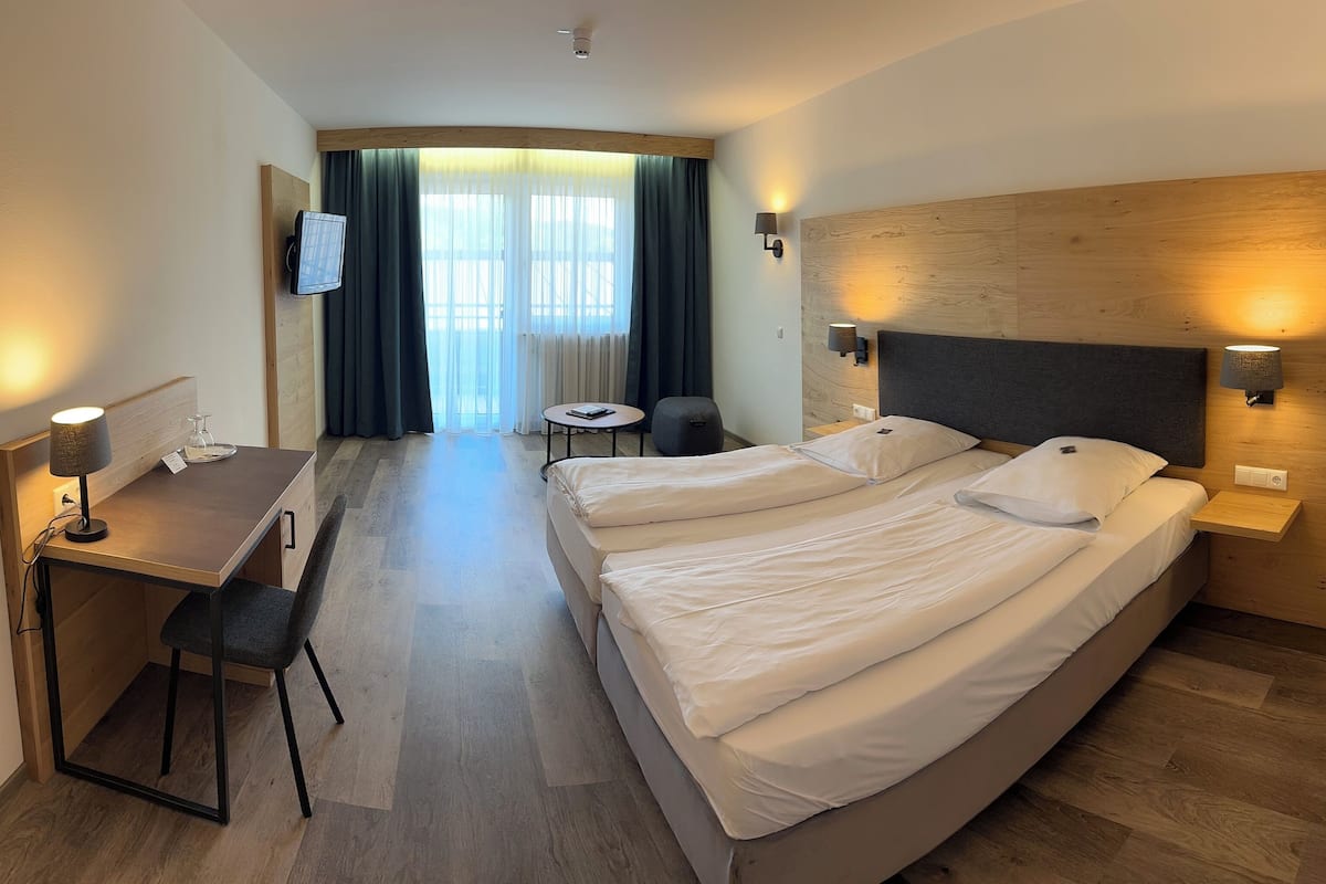 A hotel room with a large bed, a desk with a chair, a small table, and a TV mounted on the wall.