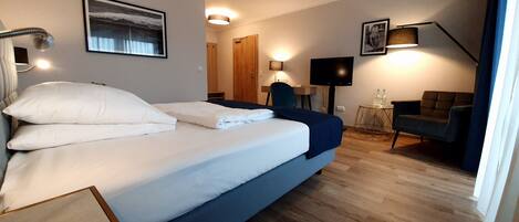 A hotel room with a bed, a television, a chair, and a small table with two bottles.