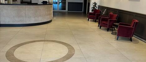 A hotel lobby with a reception desk, seating area, and a decorative carpet with text.