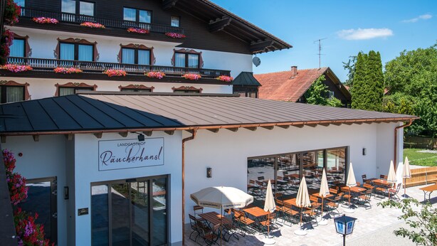 A restaurant with outdoor seating, a sign reading "Landgasthof Räucherl", and a building with balconies adorned with flowers.