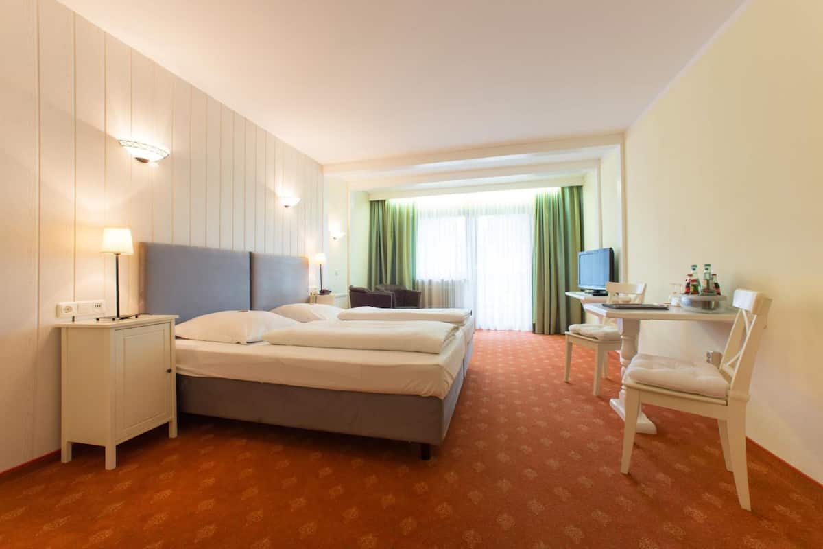 A hotel room with a bed, a desk with a chair, a TV, and a window with curtains.