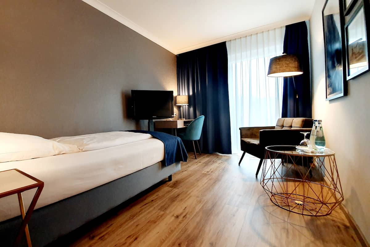 A hotel room with a bed, a desk, a chair, a TV, and a lamp.