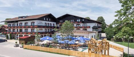 A traditional European hotel with multiple balconies, outdoor seating, and a wooden play structure.
