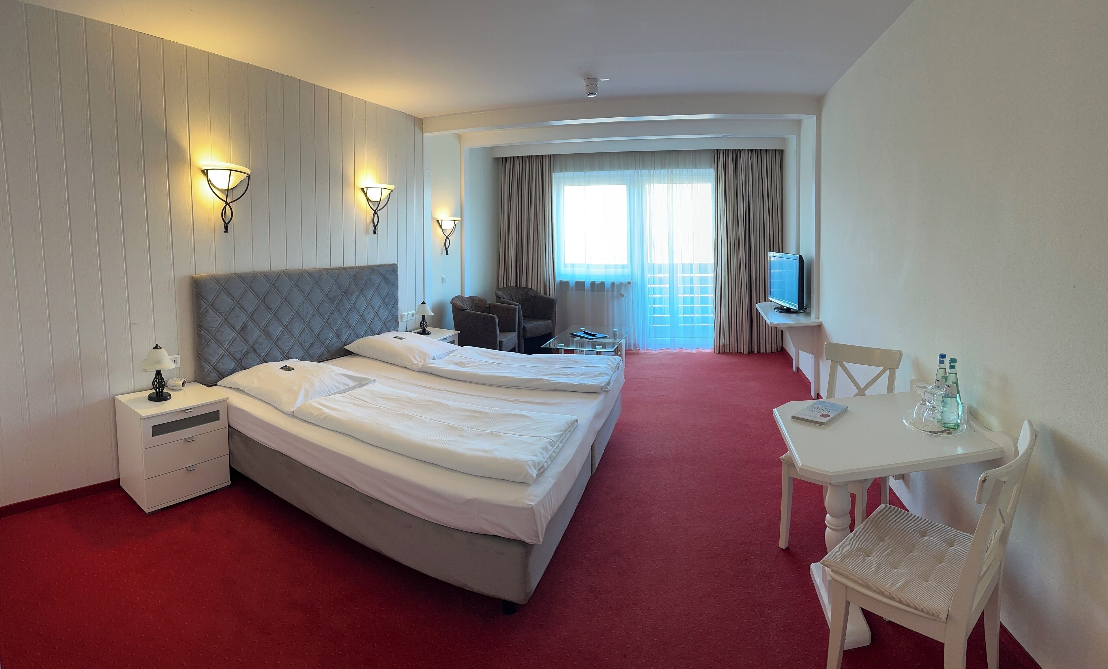 A hotel room with two beds, a desk, a chair, a TV, and a window with curtains.