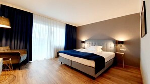 A modern hotel room with a large bed, a sofa, and a desk.