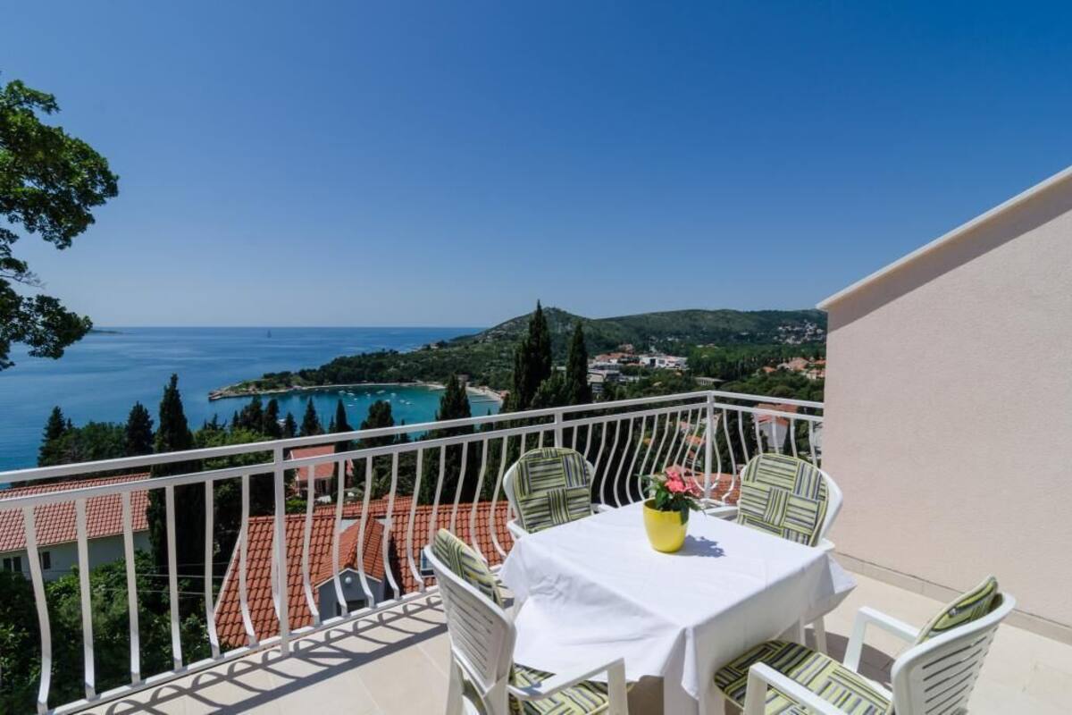 A balcony with a table and chairs overlooking a coastal view with a pool and buildings.