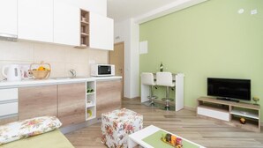 A modern living room with a flat-screen TV, a dining area with two white chairs, a kitchen with white cabinets and a microwave, and a green accent wall. - Apartments Marmo (Zupa dubrovacka)