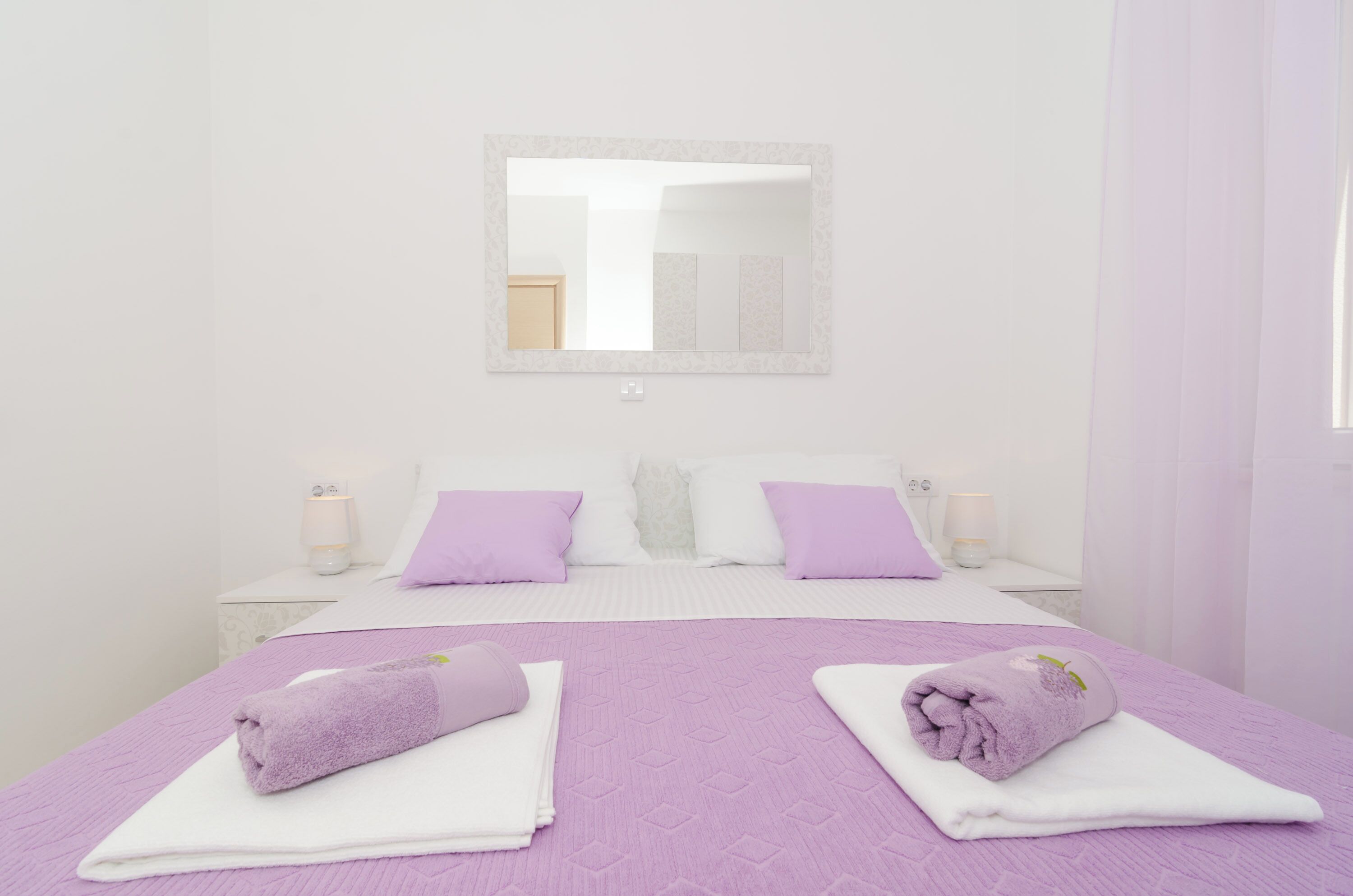 A hotel room with a large bed, two nightstands, a mirror, and a window with curtains.